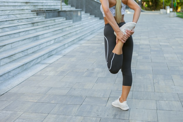 Jonge slanke fitnessvrouw in sportkleding die rek- en opwarmingsoefeningen doet voor het been voordat ze buitenshuis gaat trainen