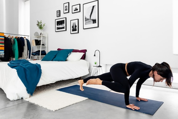 Jonge slanke vrouw beoefenen van yoga in moderne minimalistische slaapkamer thuis