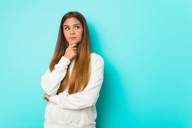 Jonge slanke vrouw die zijdelings met twijfelachtige en sceptische uitdrukking kijkt.