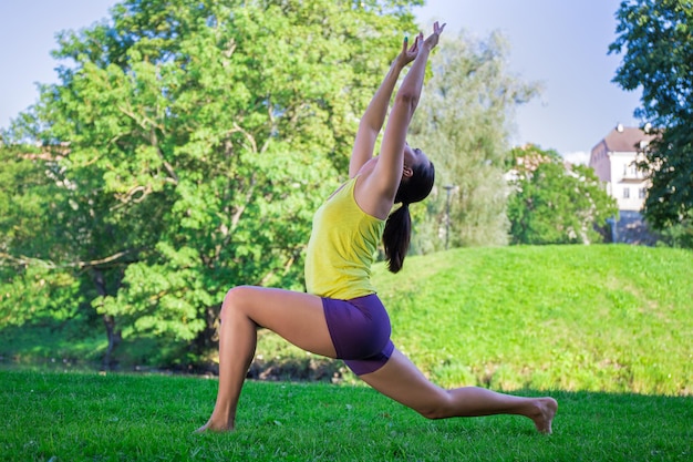 Jonge slanke vrouw doet yoga-oefeningen in park wassende maan pose