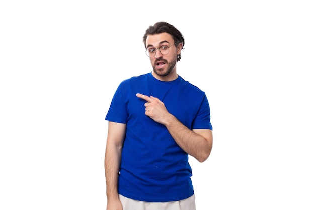Jonge slimme blanke man met donker goed verzorgd haar en baard in een blauw T-shirt wijst zijn hand naar