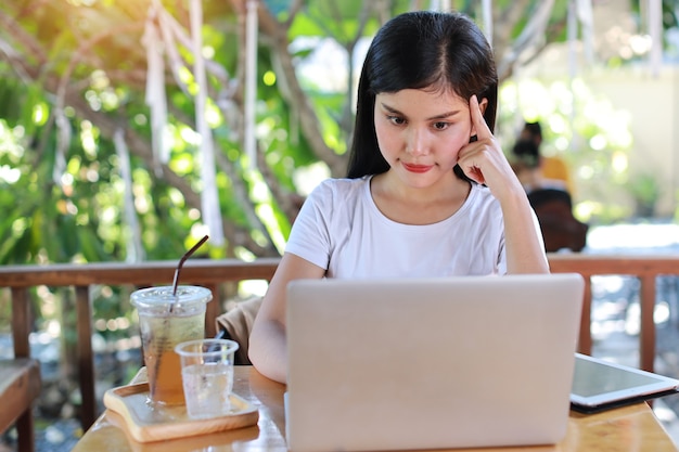 Jonge slimme en actieve aziatische vrouwelijke student die zit en computer gebruikt, nota neemt van online studeren met een blij lachend gezicht (nieuw normaal concept)