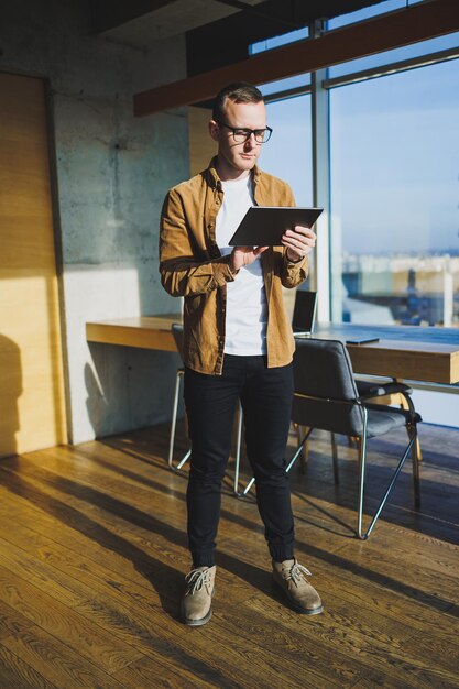 Jonge slimme freelancer in casual kleding en bril werken op tablet werken met documenten en laptopcomputer aan tafel Een student die online studeert met een netbook