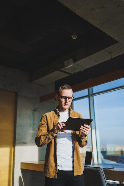 Jonge slimme freelancer in casual kleding en bril werken op tablet werken met documenten en laptopcomputer aan tafel Een student die online studeert met een netbook