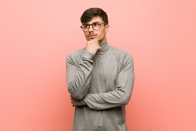 Jonge slimme studentenmens die zijdelings met twijfelachtige en sceptische uitdrukking kijkt.
