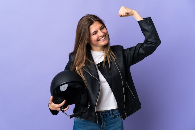 Jonge slowaakse vrouw die een motorhelm houdt die op purpere achtergrond wordt geïsoleerd die een overwinning viert