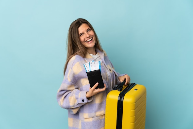 Jonge Slowaakse vrouw die op blauwe muur in vakantie met koffer en paspoort wordt geïsoleerd