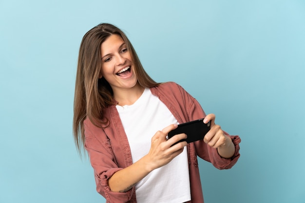 Jonge slowaakse vrouw geïsoleerd op blauwe achtergrond spelen met de mobiele telefoon