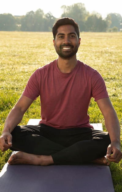 Jonge smiley man buiten mediteren op yoga mat