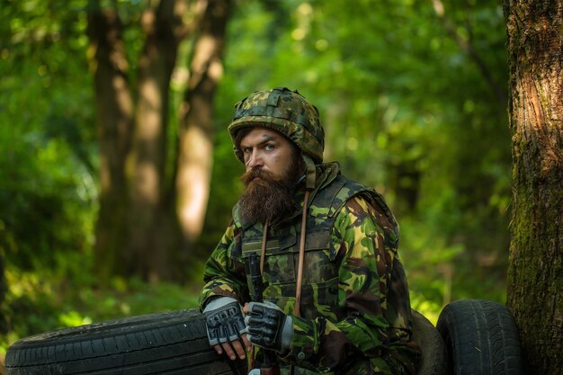 Jonge soldaat met bebaarde stoffige vermoeide gezicht in militair camouflage-uniform met hangende camera en r