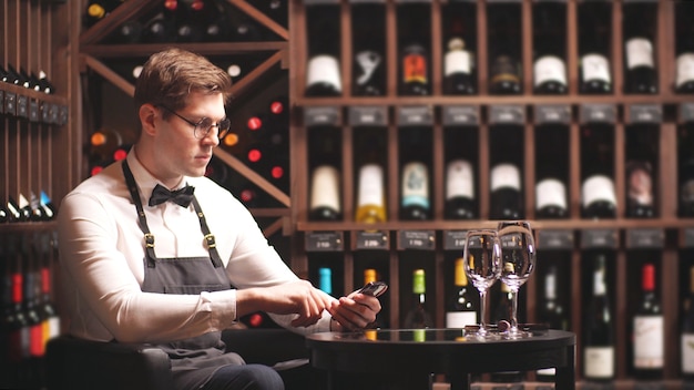 Jonge sommelier maakt aantekeningen op zijn smartphone om in een wijnboetiek te werken