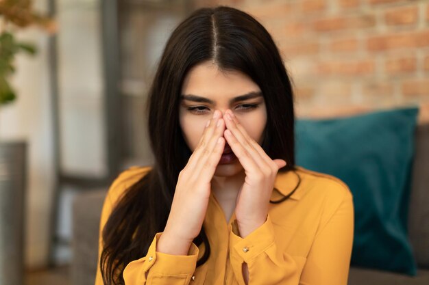 Jonge spaanse dame die haar neusbrug aanraakt en lijdt aan rhinitis, seizoensgebonden allergie of antritis