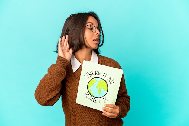 Jonge Spaanse gemengde rasvrouw die een planeet houdt sparen aanplakbiljet dat probeert een roddel te luisteren.