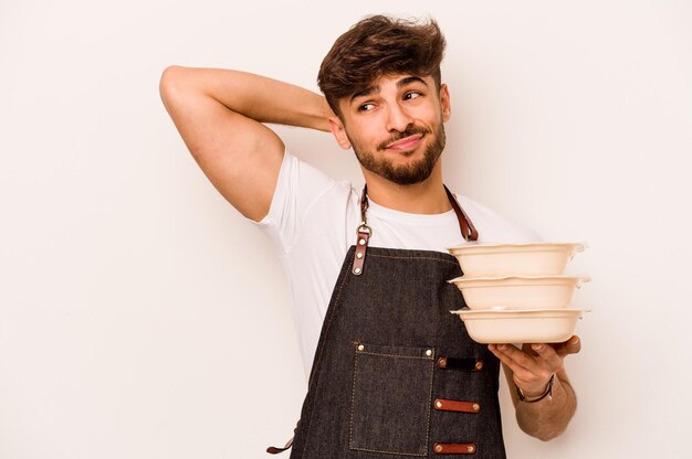 Jonge Spaanse klerk man met een tupperware geïsoleerd op een witte achtergrond aanraken achterkant hoofd denken en een keuze maken