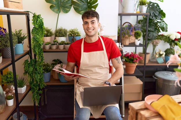 Jonge spaanse man bloemist met behulp van laptop leesboek bij bloemenwinkel