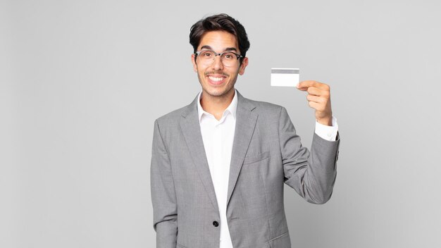 Jonge Spaanse man die er blij en aangenaam verrast uitziet en een creditcard vasthoudt
