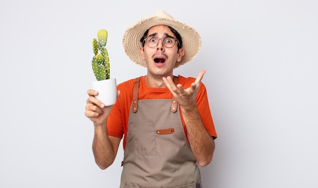 Jonge spaanse man die er wanhopig, gefrustreerd en gestrest uitziet. tuinman met cactusconcept