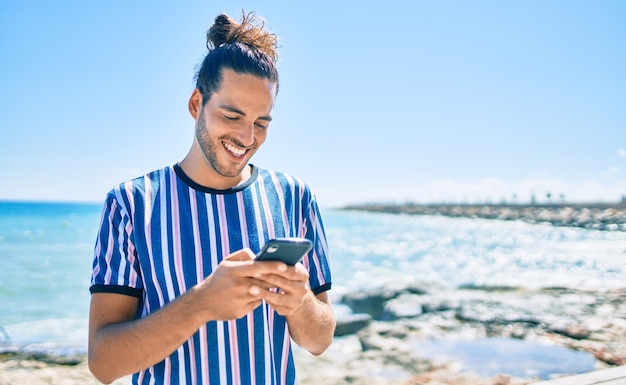 Jonge Spaanse man die gelukkig glimlacht met zijn smartphone op het strand