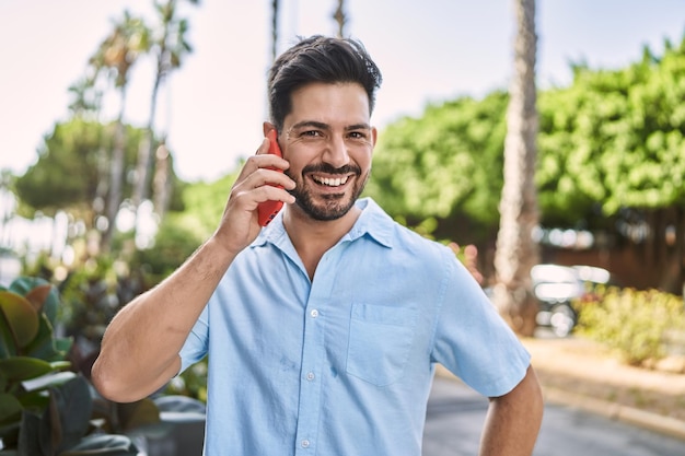 Jonge spaanse man die lacht gelukkig praten op de smartphone in de stad.