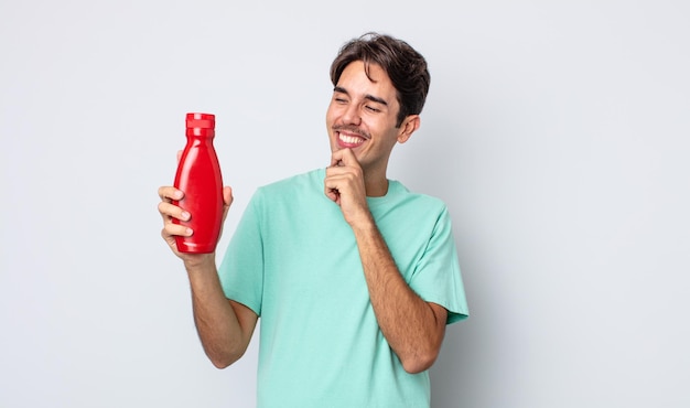 Jonge spaanse man die lacht met een gelukkige, zelfverzekerde uitdrukking met de hand op de kin. ketchup concept