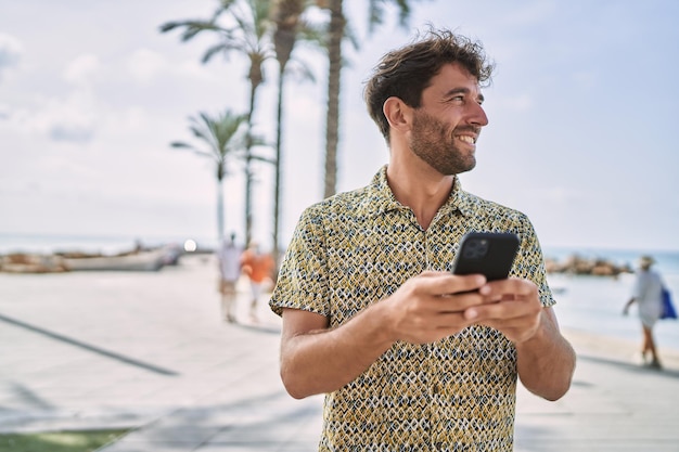 Jonge Spaanse man die lacht zelfverzekerd met behulp van smartphone aan zee