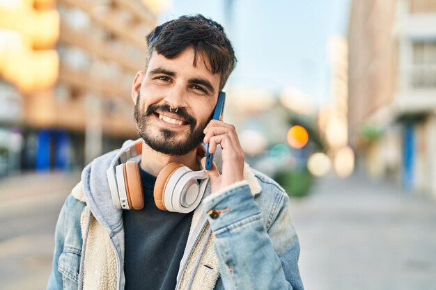 Jonge spaanse man die op de smartphone praat met een koptelefoon op straat