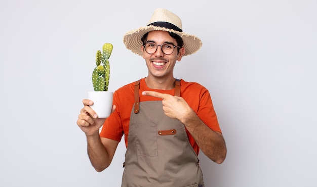 Jonge spaanse man die opgewonden en verrast kijkt en naar de zijkant wijst. tuinman met cactusconcept