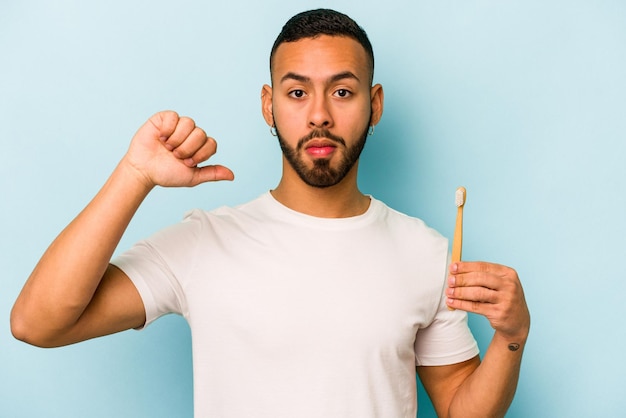 Jonge Spaanse man die tanden poetst geïsoleerd op blauwe achtergrond voelt zich trots en zelfverzekerd voorbeeld om te volgen