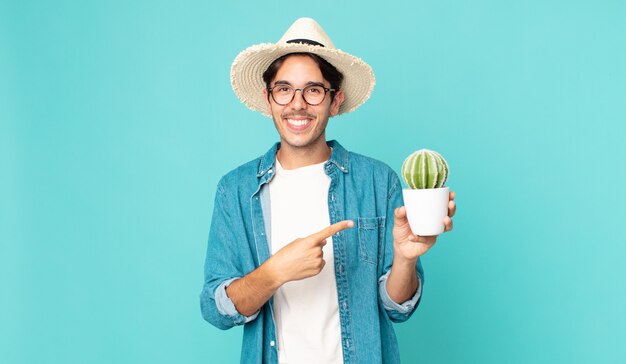 Jonge Spaanse man die vrolijk lacht, zich gelukkig voelt en naar de zijkant wijst en een cactus vasthoudt