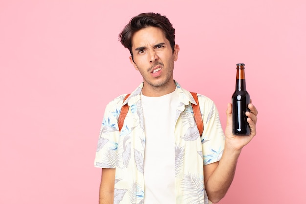 Jonge Spaanse man die zich verbaasd en verward voelt en een flesje bier vasthoudt