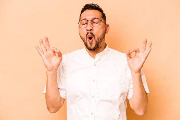 Jonge Spaanse man geïsoleerd op een beige achtergrond ontspant zich na een harde werkdag die ze yoga aan het uitvoeren is