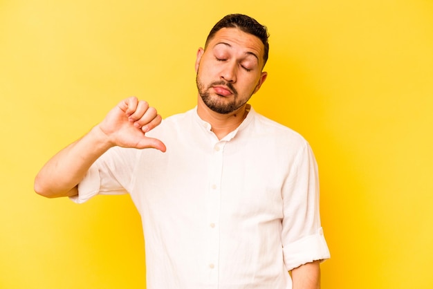 Jonge Spaanse man geïsoleerd op gele achtergrond met een afkeer gebaar duimen omlaag meningsverschil concept
