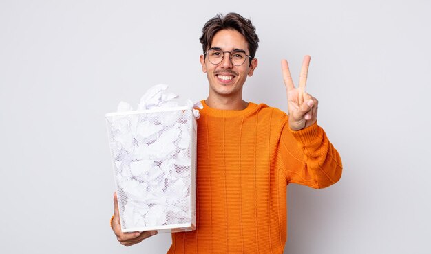 Jonge Spaanse man lacht en ziet er vriendelijk uit, met nummer twee. papier ballen prullenbak concept