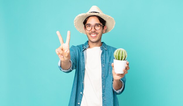 Jonge Spaanse man lacht en ziet er vriendelijk uit, toont nummer twee en houdt een cactus vast