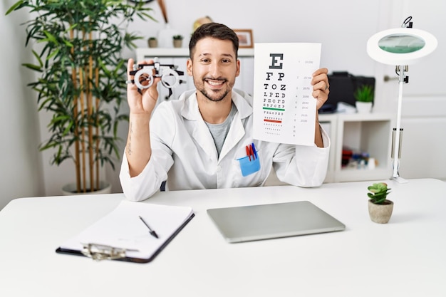 Jonge spaanse man met opticien uniform met snellen-test in de kliniek