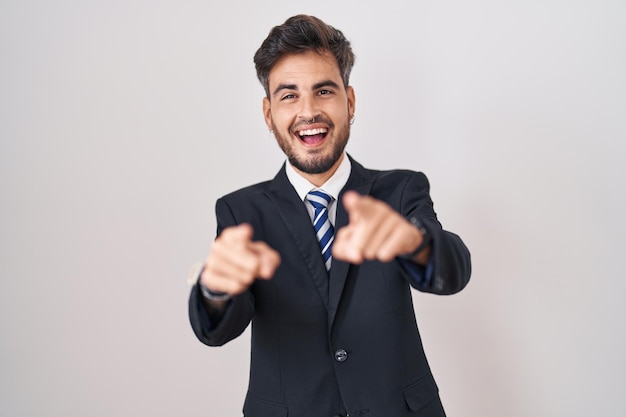 Jonge spaanse man met tatoeages in pak en stropdas die naar jou en de camera wijst met vingers die positief en opgewekt glimlachen