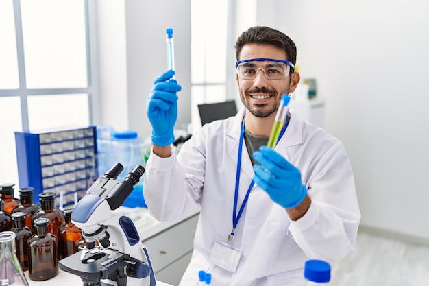 Jonge spaanse man met wetenschapper uniforme reageerbuisjes in het laboratorium