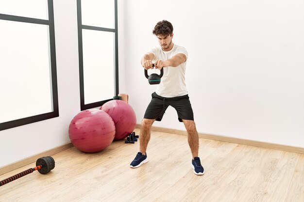 Jonge Spaanse man traint met kettlebell in het sportcentrum