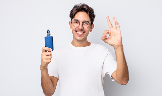 jonge spaanse man voelt zich gelukkig en toont goedkeuring met een goed gebaar. rook verdamper concept