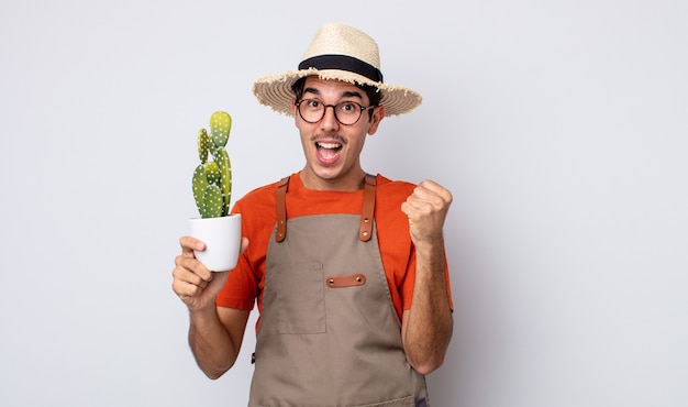 Jonge spaanse man voelt zich geschokt, lacht en viert succes. tuinman met cactusconcept