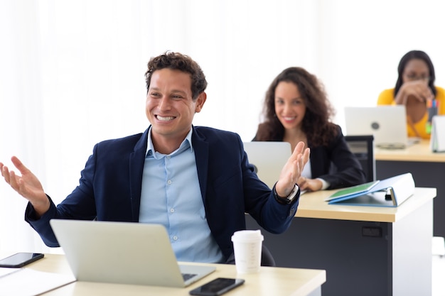 Jonge Spaanse man zit koffie te drinken en werkt op laptopcomputer op creatieve kantoor aan huis.