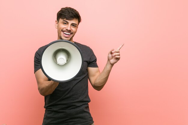 Jonge Spaanse mens die een megafoon houden glimlachend vrolijk wijzend met weg wijsvinger.