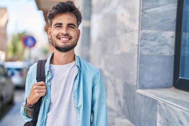 Jonge Spaanse student die zelfverzekerd glimlacht met rugzak op straat