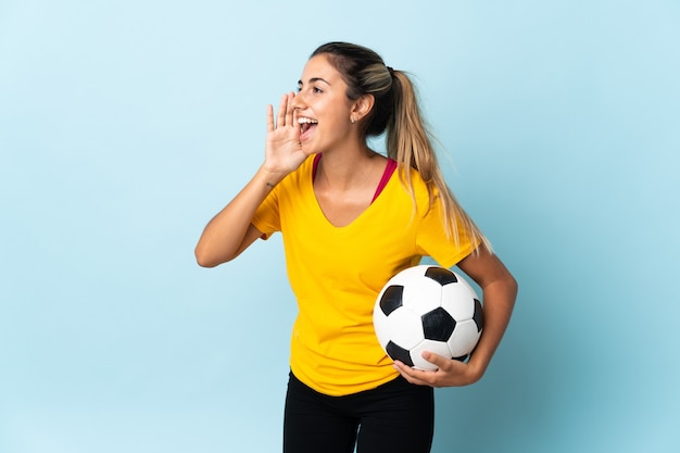 Jonge Spaanse voetballervrouw over geïsoleerd op blauw schreeuwen met wijd open mond aan de kant