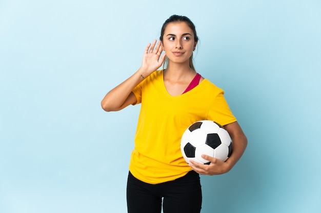 Jonge Spaanse voetballervrouw over geïsoleerd op blauwe muur die twijfels hebben