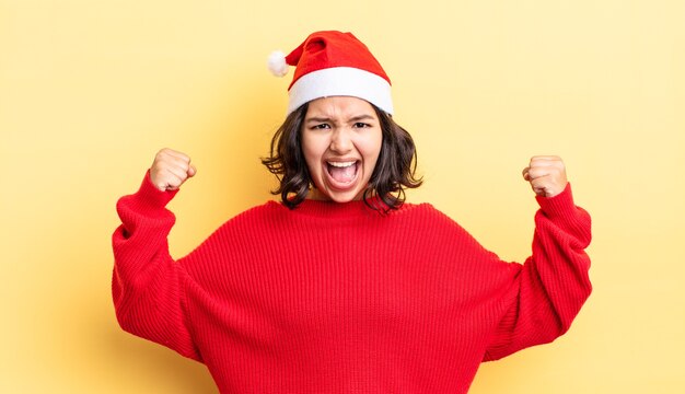 Jonge Spaanse vrouw die agressief schreeuwt met een boze uitdrukking. kerst concept