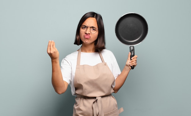 Jonge Spaanse vrouw die capice of geldgebaar maakt en u vertelt om uw schulden te betalen!