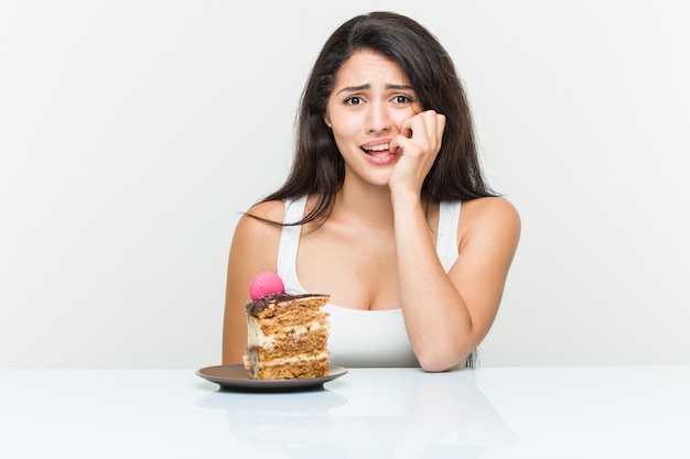 Jonge Spaanse vrouw die een cake eet die vingernagels bijt, zenuwachtig en zeer bezorgd.