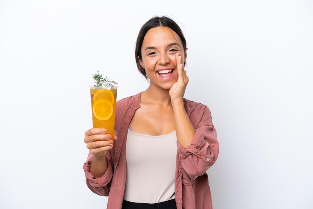 Jonge spaanse vrouw die een cocktail houdt die op witte achtergrond wordt geïsoleerd die met wijd open mond schreeuwt