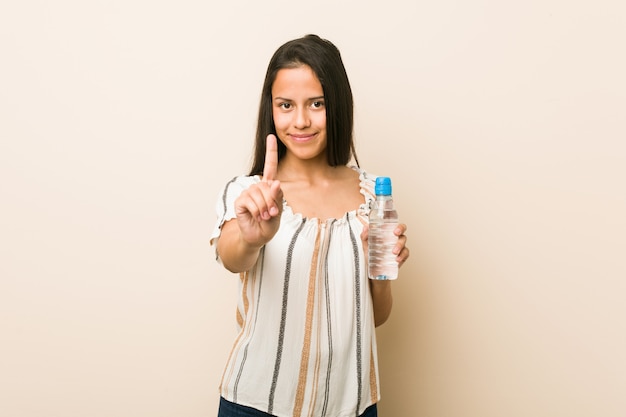 Jonge Spaanse vrouw die een fles water houdt dat nummer één met vinger toont.